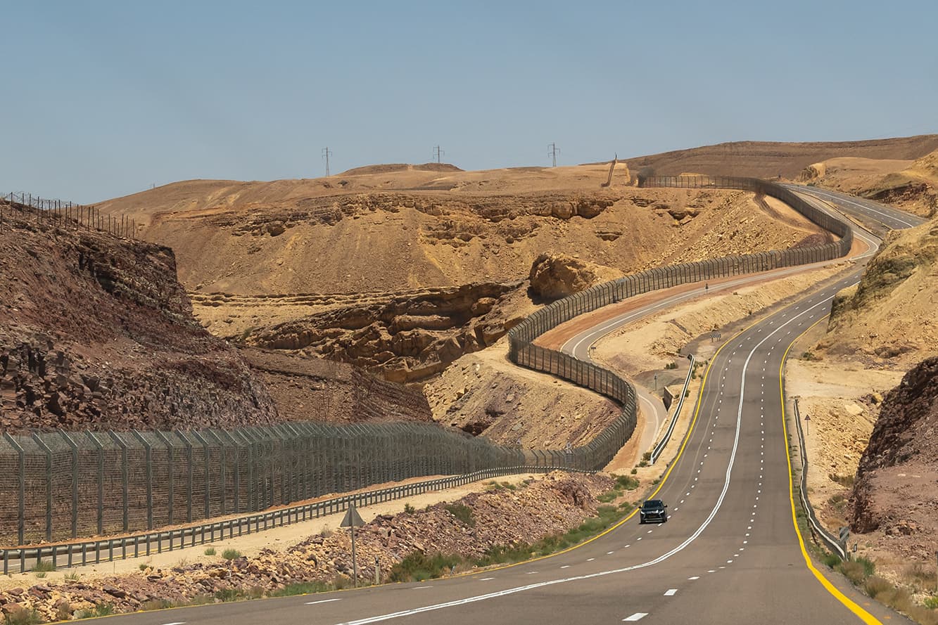 Highway through the Negev Desert on the border with Egypt showing the fence between the countries in Southern Israel Highway through the Negev Desert on the border with Egypt showing the fence between the countries in Southern Israel